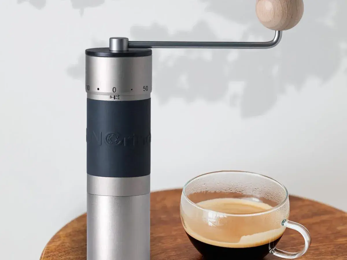 KINGrinder K6 hand grinder on a wooden table next to a glass cup of coffee