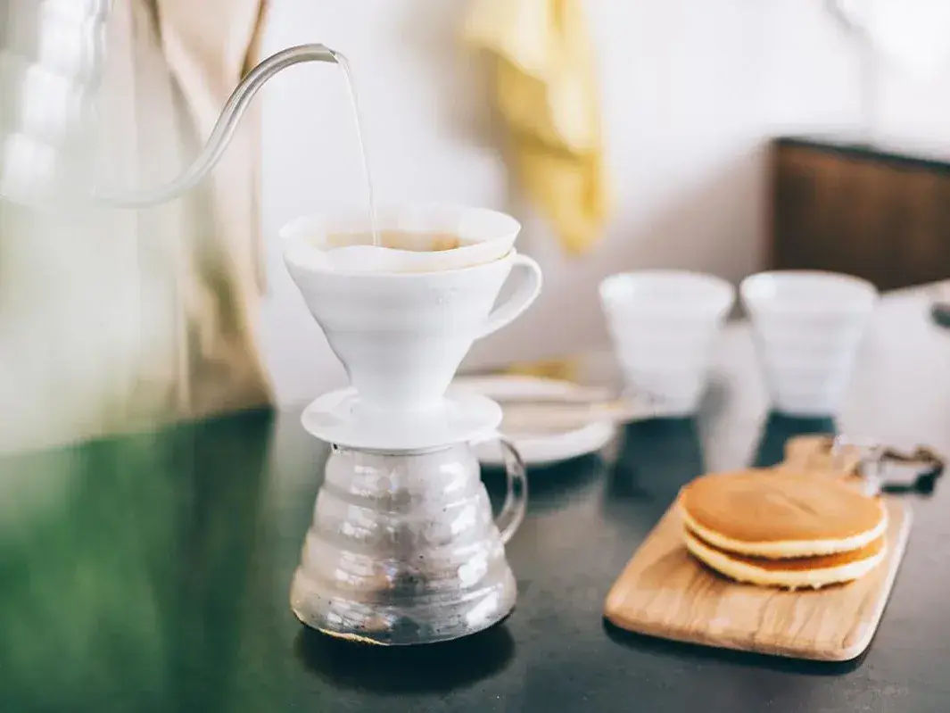 Hario V60 dripper and glass server on a wooden board next to a plate of pancakes