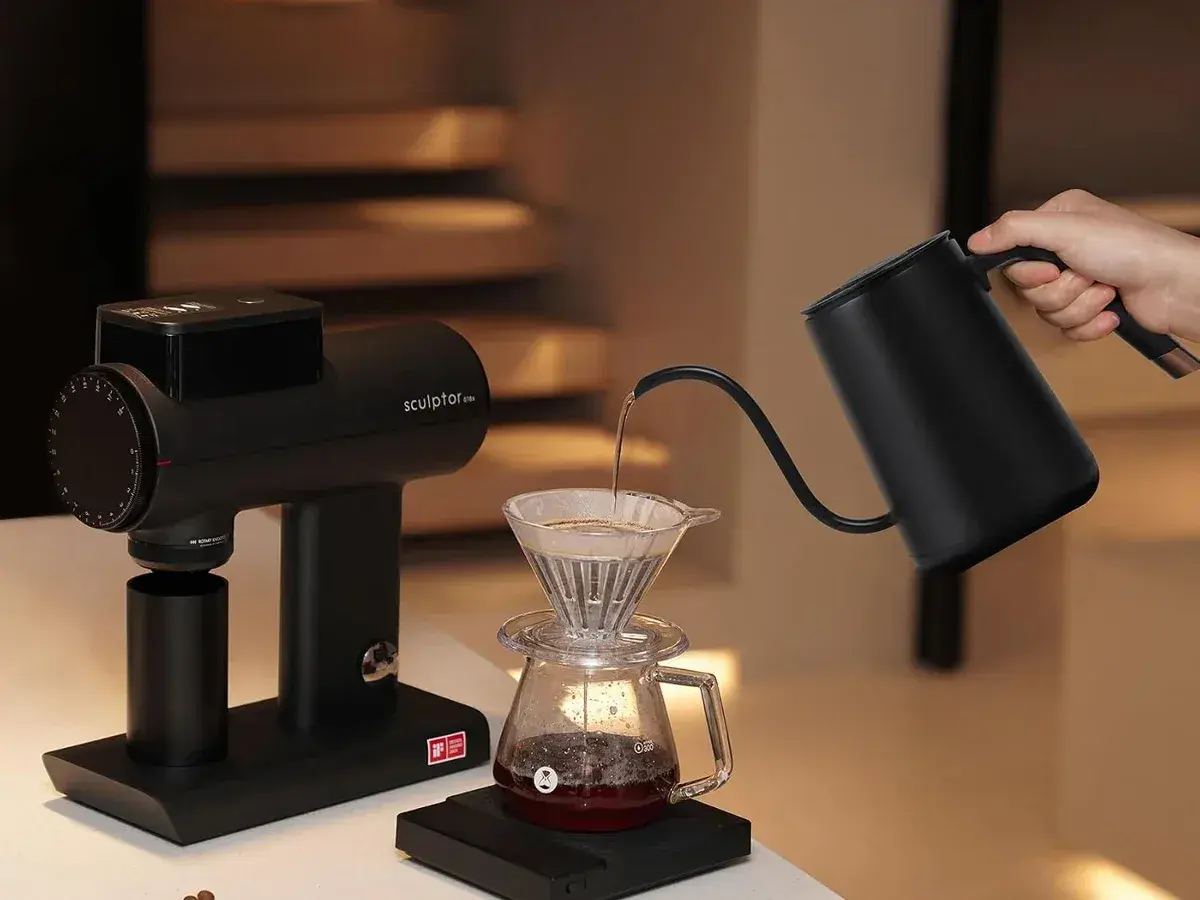Timemore Fish gooseneck kettle pouring over a dripper in a dim kitchen